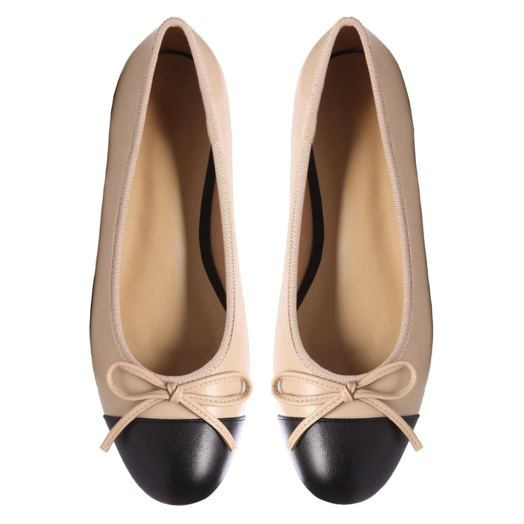 Beige and black ballet flats with a chic black cap toe and bow embellishment.